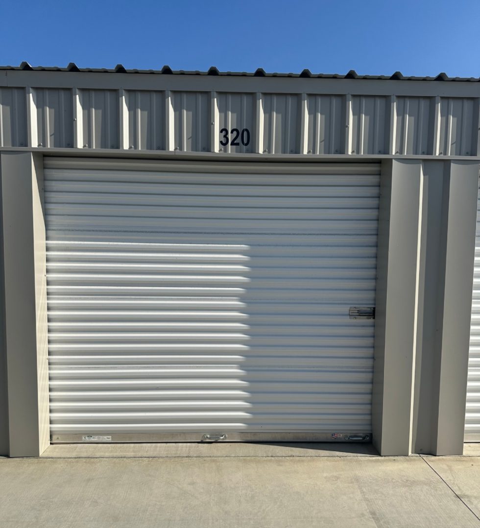 Close up view of a secure metal roll up door on a clean drive up access self storage unit labeled number 320 at a locally operated Visalia facility.