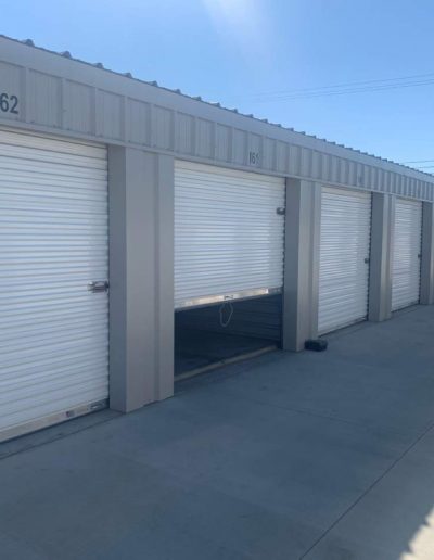 A row of well-maintained self-storage units with white roll-up doors and numbered headers, featuring a wide concrete driveway for easy vehicle access.