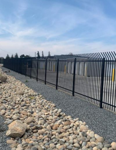 A long, clean concrete driveway between two rows of gray metal self-storage units with white roll-up doors and yellow protective bollards.
