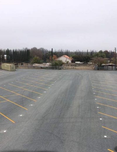 A secure, high black metal fence with curved top pickets bordering a landscape of smooth river rocks and gravel, protecting the storage facility interior.