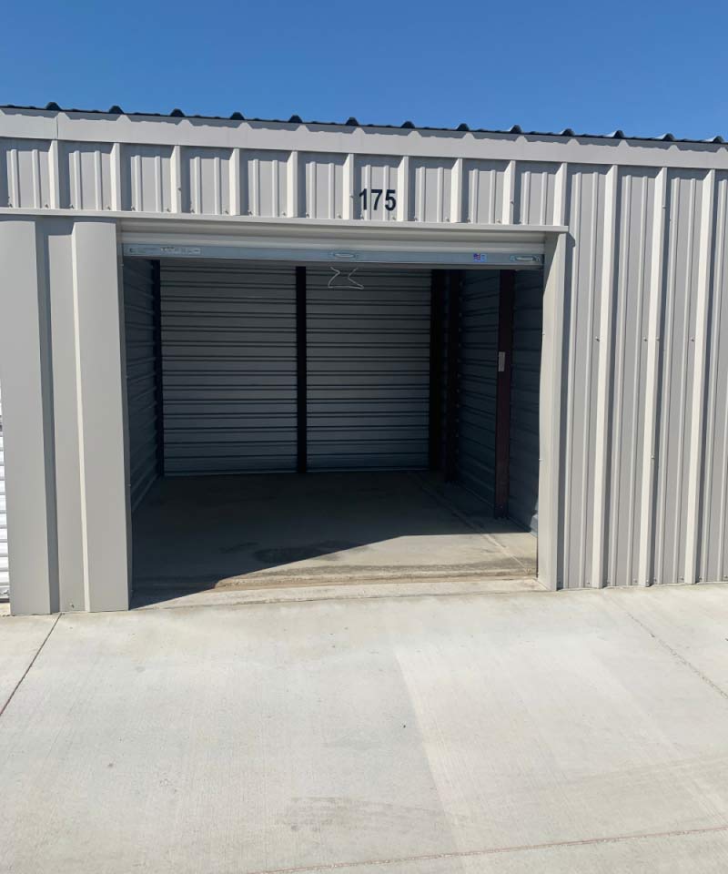 An open, drive-up self-storage unit in Visalia, showing a clean, empty concrete interior and a secure metal roll-up door under a clear blue sky.
