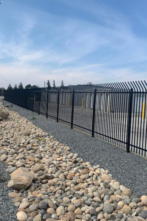 A long, clean concrete driveway between two rows of gray metal self-storage units with white roll-up doors and yellow protective bollards.